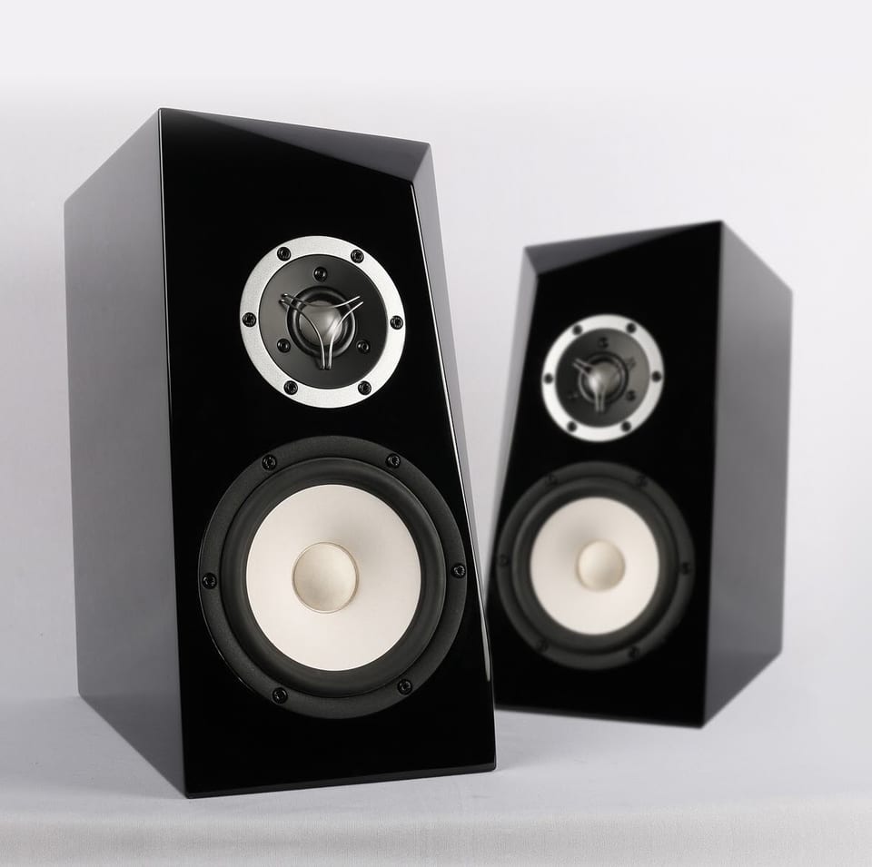 Pair of gloss black bookshelf speakers with tapered cabinets, silver-rimmed dome tweeter above a cream cone woofer