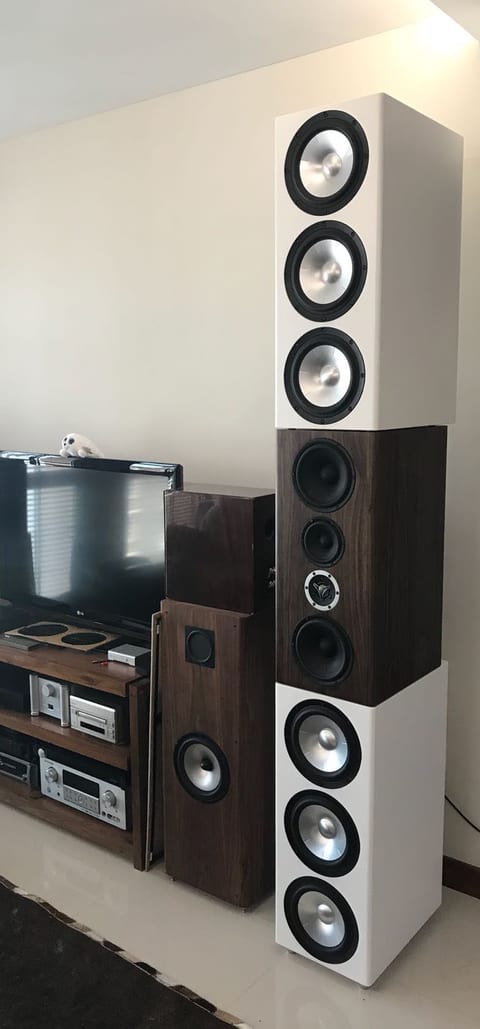 Satori Statement line array in a living room: white modules of silver-cone woofers above and below a dark wood module.