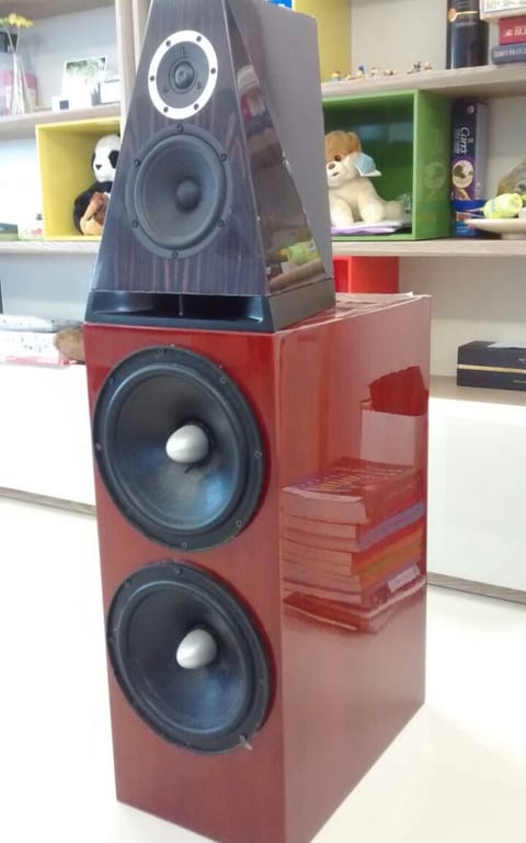 Trapezium head unit with tweeter and midwoofer on a red gloss bass cabinet holding two large woofers, in a room.