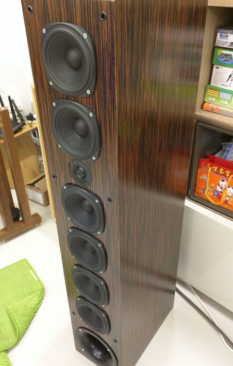 Uluwatu floorstander in dark striped gloss veneer: six small midwoofers around a tweeter, port at the base