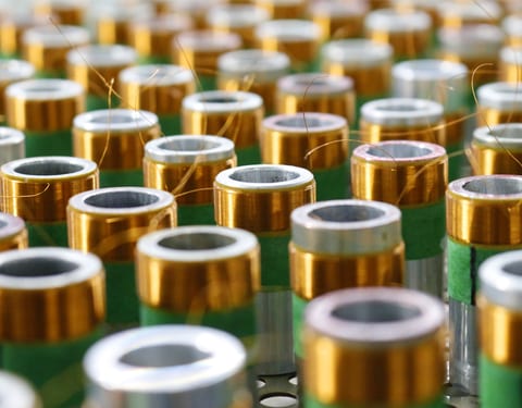 Close-up of finished voice coils standing in rows: copper and gold wire wound onto green and silver formers, with the lead-out wires still standing proud.